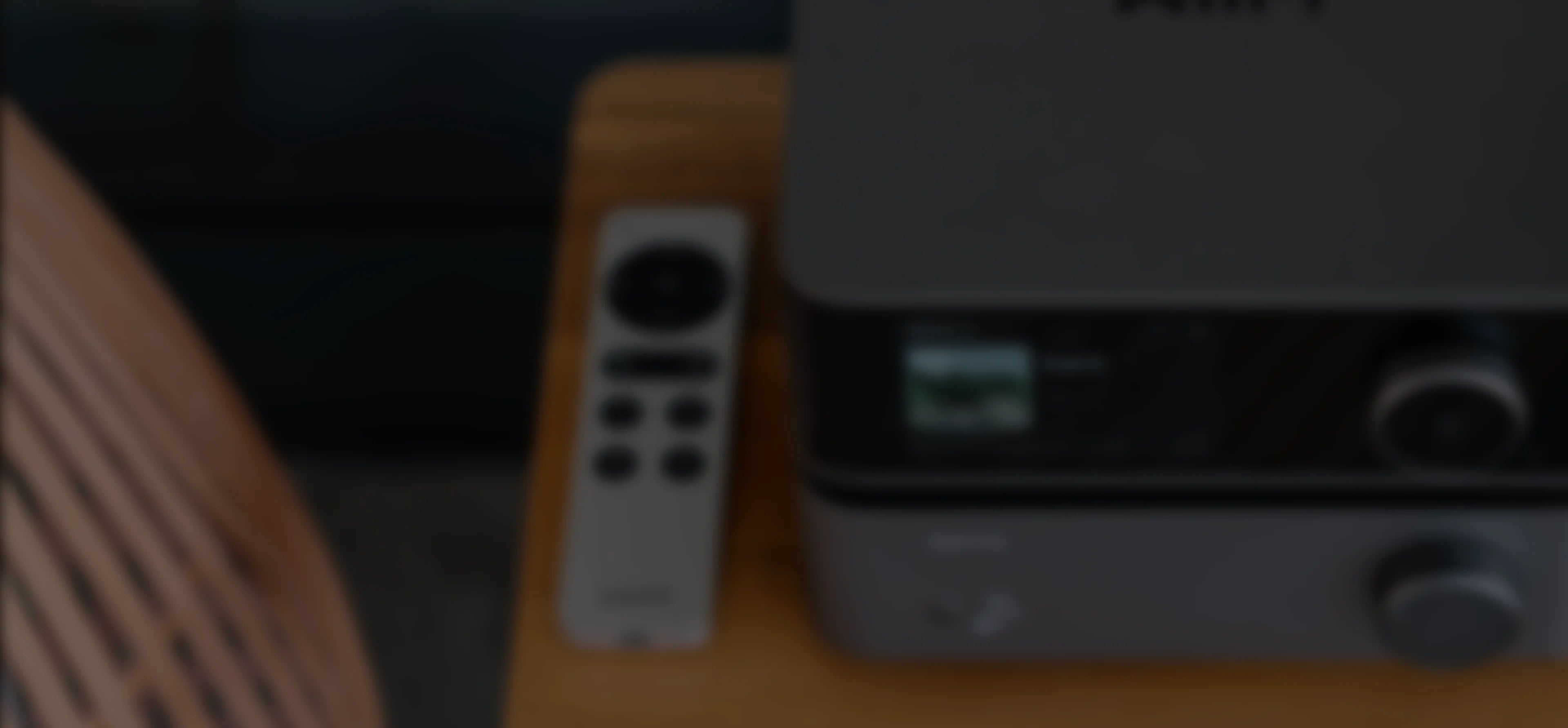 WiiM remote control placed on a wooden table next to a WiiM audio device, showing home audio setup