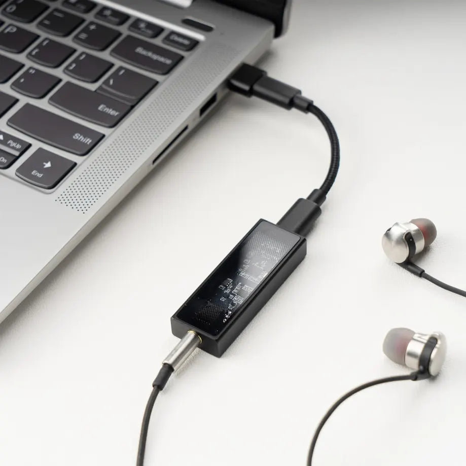 Questyle M12i portable DAC and headphone amplifier connected to a laptop via USB-C, powering wired in-ear earphones.